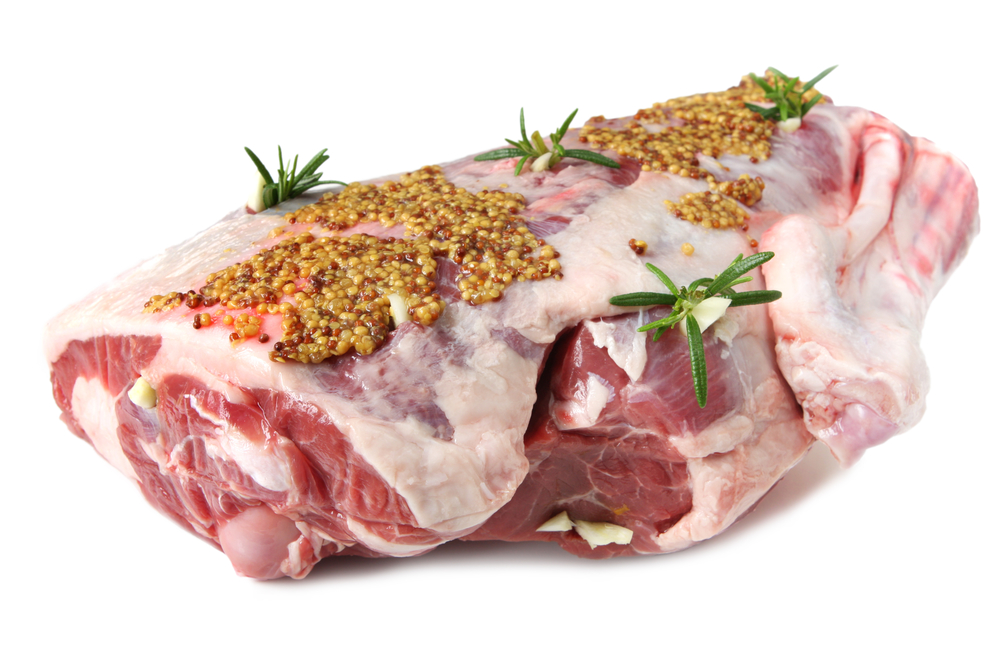 Leg of lamb cut ready for roasting, studded with garlic and fresh rosemary, and covered in seeded mustard.